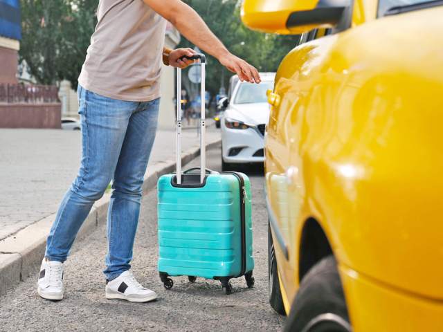 Traveler stepping into yellow taxi cab with luggage