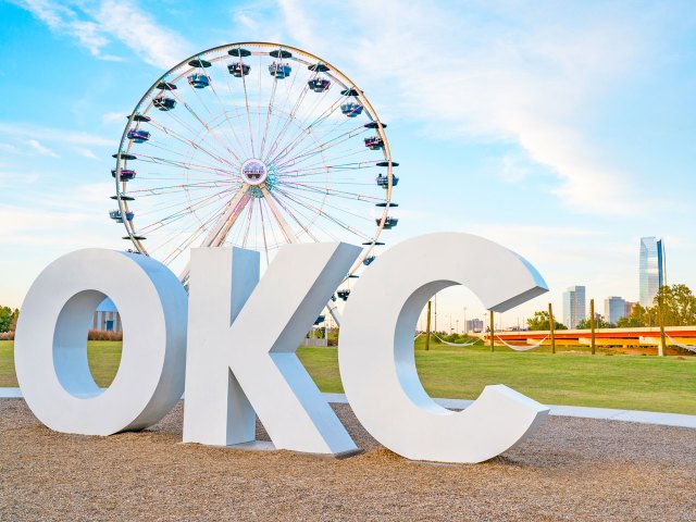 Large "OKC" block letters in park with Ferris wheel in Oklahoma City