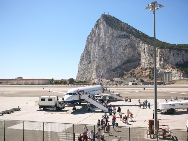 Passengers boarding aircraft via air stairs at Gibraltar International Airport with Rock of Gibraltar in background