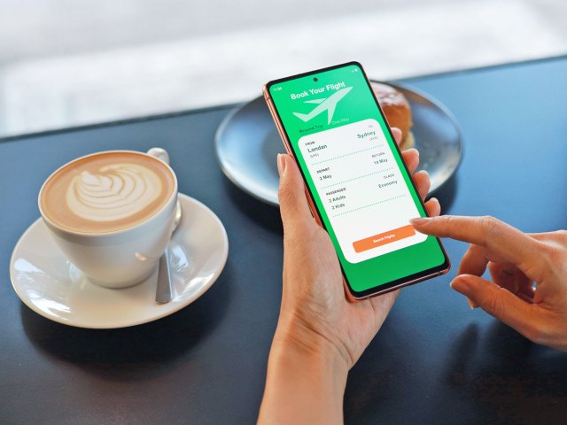 Traveler using flight booking app with cup coffee on table