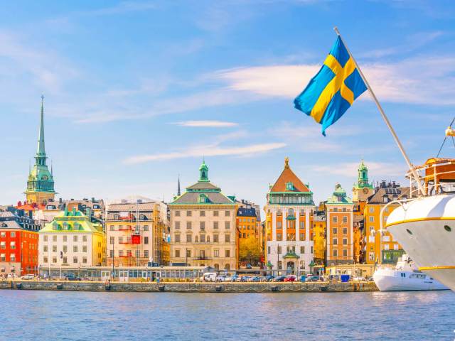 Swedish flag on boat with colorful buildings seen across river in Stockholm