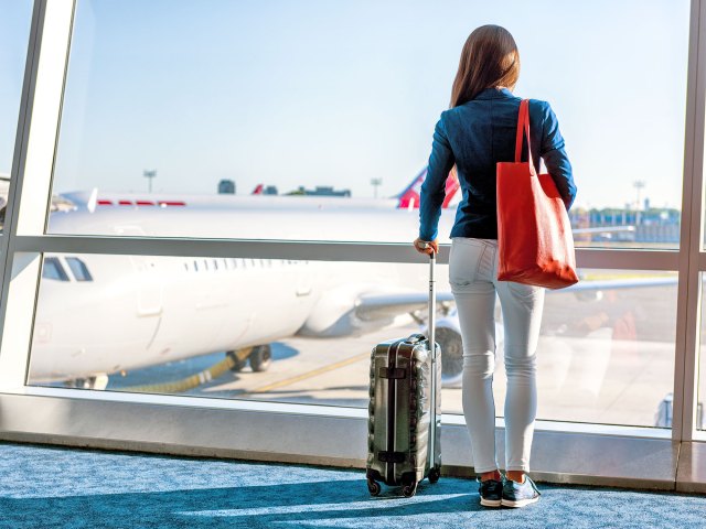 Woman with suitcase looking at airplane out of airport terminal window