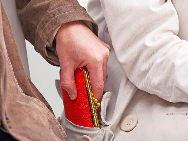 Close-up image of person taking red wallet out of another person's pocket