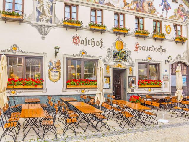 Empty sidewalk tables in front of Germany's Gasthof Fraundorfer inn, covered in Bavarian murals