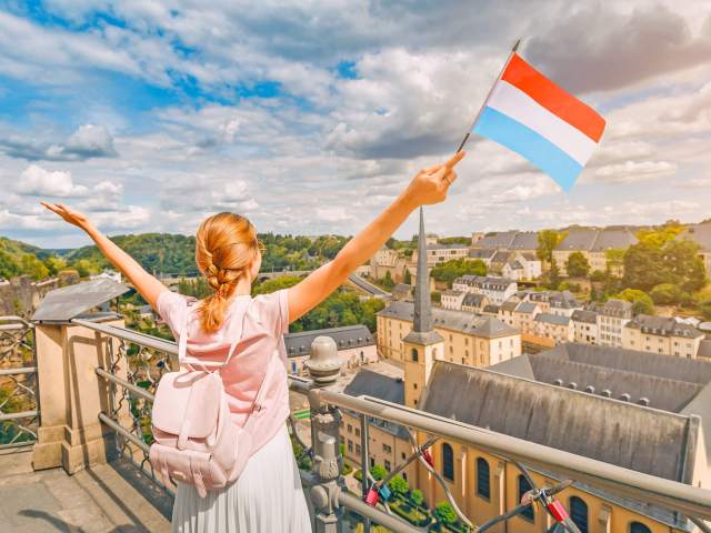 Tourist waving Luxembourg flag from balcony overlooking city skyline