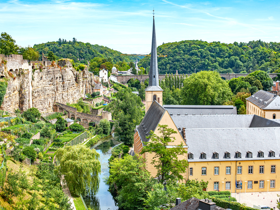 Aerial view of church tower in village surrounded by green hills in Luxembourg