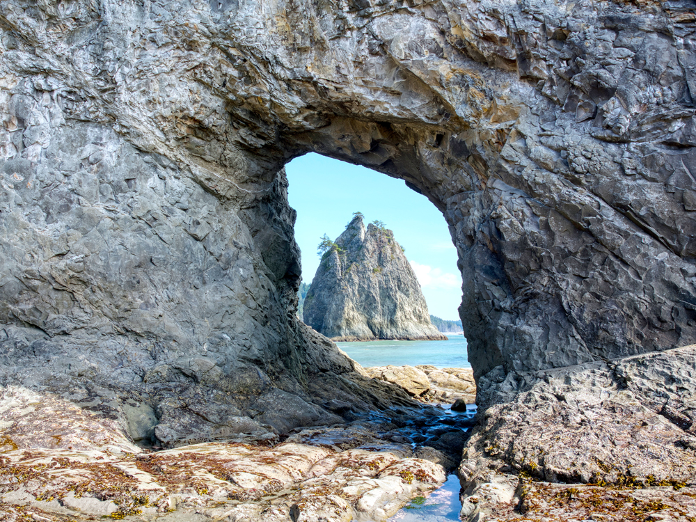 View through natural rock arch at Hole in the Wall Beach in Washington state