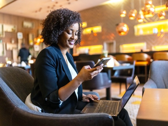 Traveler sitting in hotel lobby using laptop and smartphone