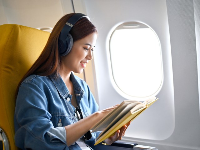 Airline passenger wearing headphones and reading book