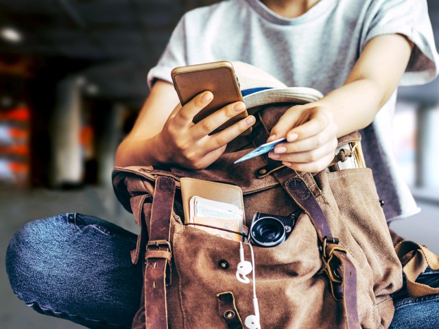 Person holding credit card and cell phone over backpack