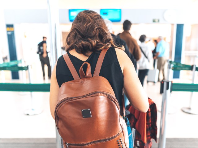 Traveler wearing backpack in airport queue, facing away from camera