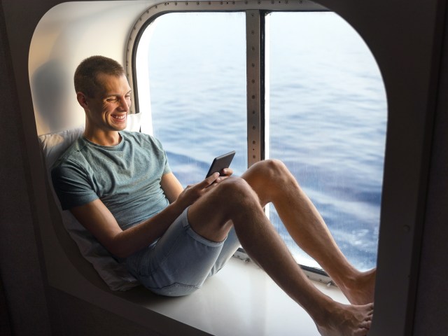 Cruise passenger reading e-book next to port window