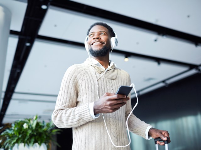 Traveler at airport wearing bulky sweater and listening to headphones