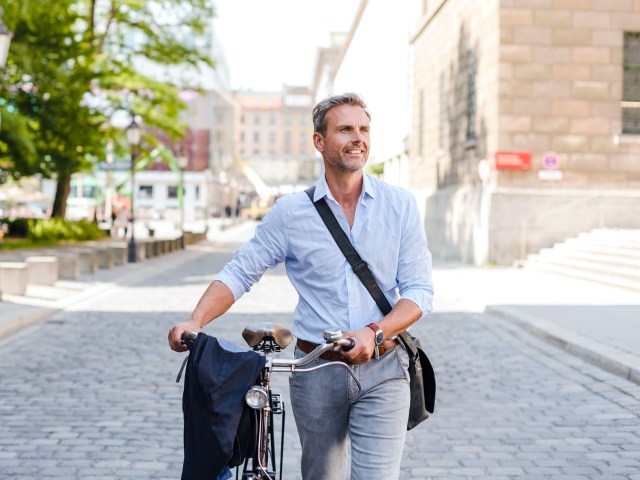 Person walking with bicycle and wearing crossbody bag