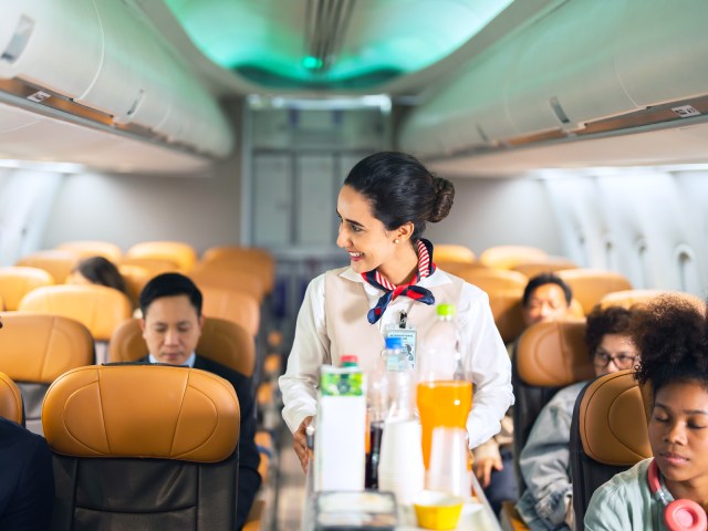 Flight attendant in airplane aisle serving passengers  from beverage cart
