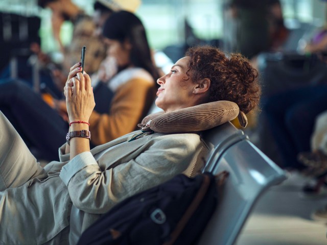 Traveler using neck pillow at airport and browsing cellphone