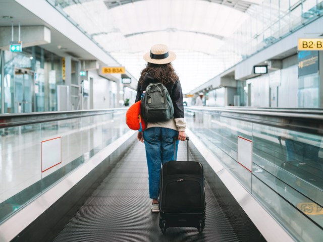 Traveler wearing backpack and rolling luggage on airport moving walkway