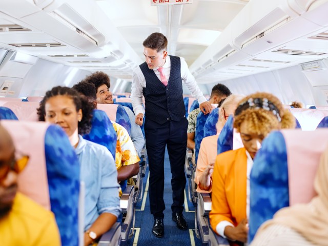 Flight attendant walking down aircraft aisle checking on passengers