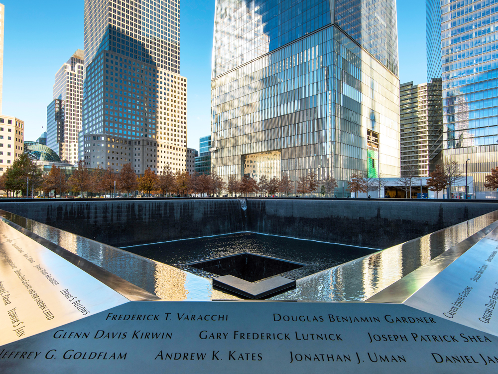 Reflecting pool of the 9/11 memorial lined with the names of victims and surrounded by downtown Manhattan skyscrapers