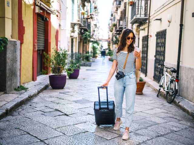 Person rolling suitcase down pedestrian street while looking at phone