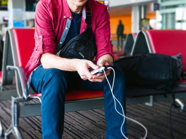 Traveler sitting at gate using portable charger to charge phone