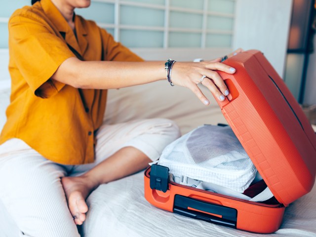 Traveler sitting on bed closing suitcase