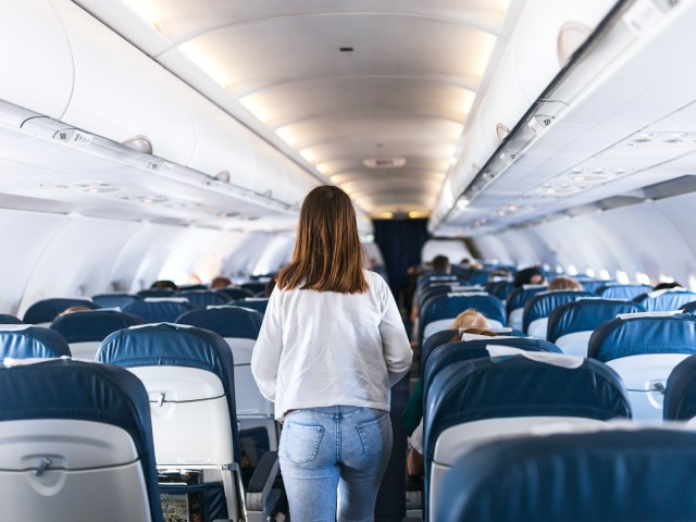 Traveler walking up airplane aisle toward front of cabin