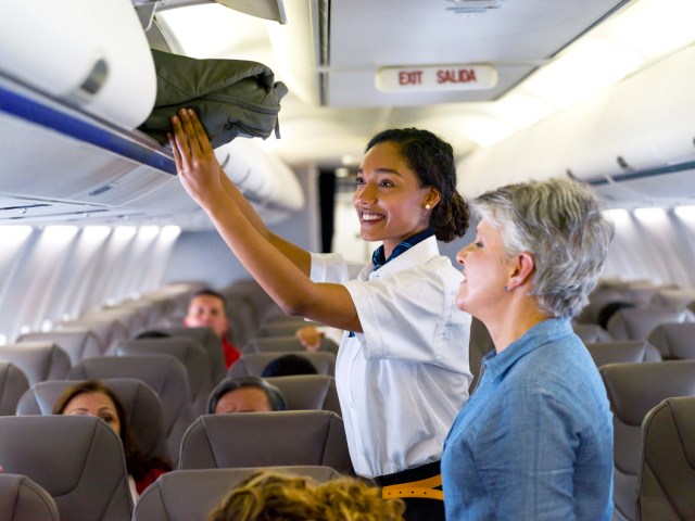 Flight attendant stowing passenger's bag in overhead bin