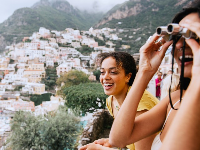 Traveler using binoculars next to companion from viewpoint in hillside city