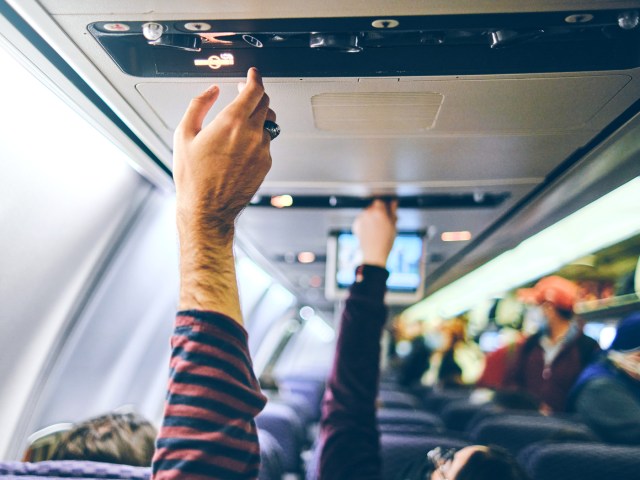 Passengers adjusting air conditioning vents with no-smoking sign visible in aircraft cabin