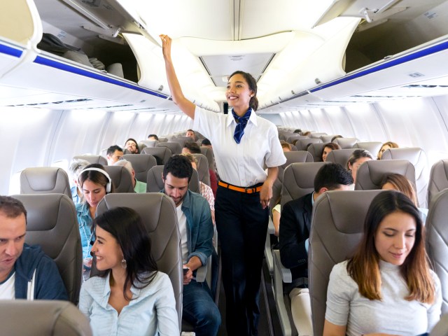 Flight attendant closing overhead bin on aircraft filled with passengers