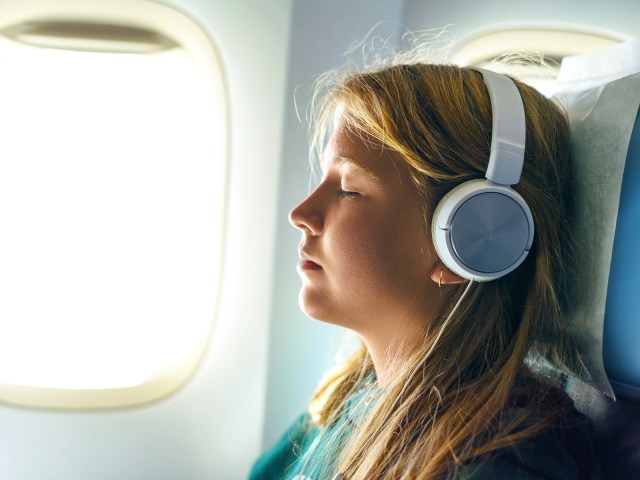 Airplane passenger in window seat sleeping while wearing headphones