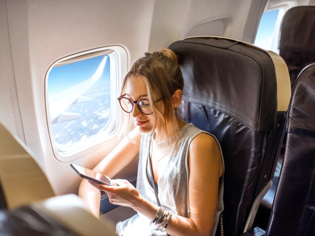 Airplane passenger sitting in window seat looking at phone