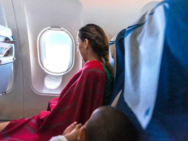 Airplane passenger wearing blanket and looking out window