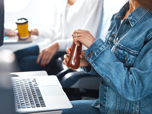 Airplane passenger with laptop on tray table and drink in hand