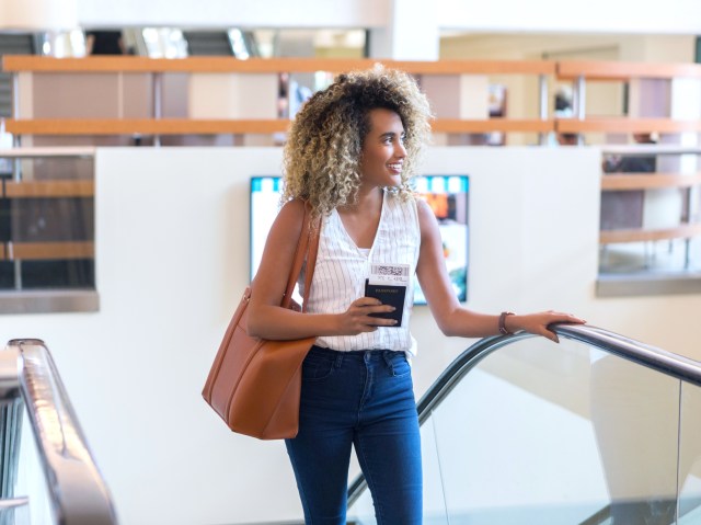 Traveler on airport escalator holding passport in hand