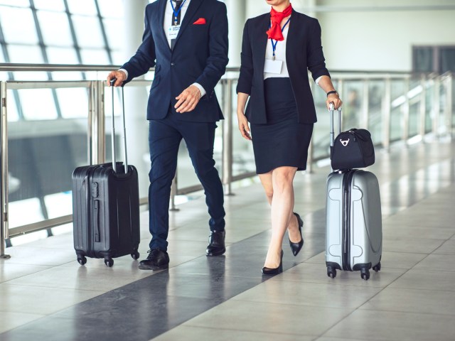 Two flight attendants rolling luggage through airport terminal