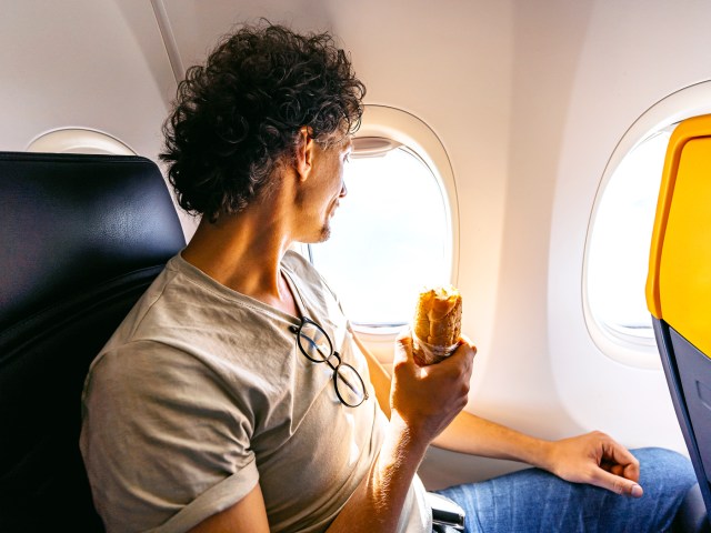 Airplane passenger holding sandwich while looking out of window