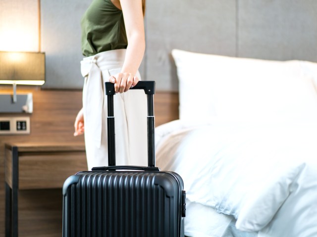 Traveler with suitcase next to bed in hotel room