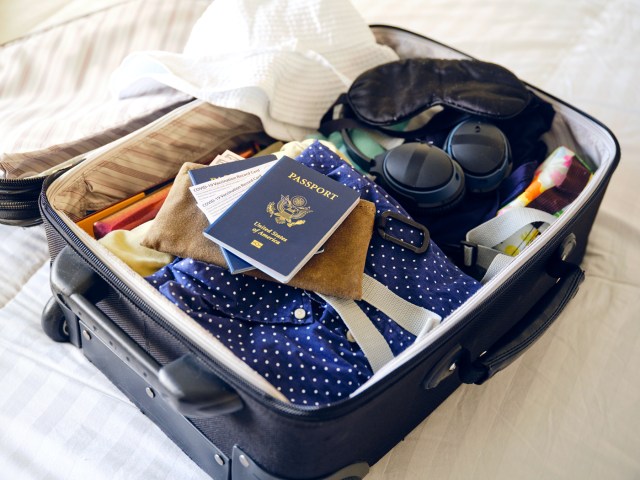 Suitcase on bed packed with clothing, accessories, and passport