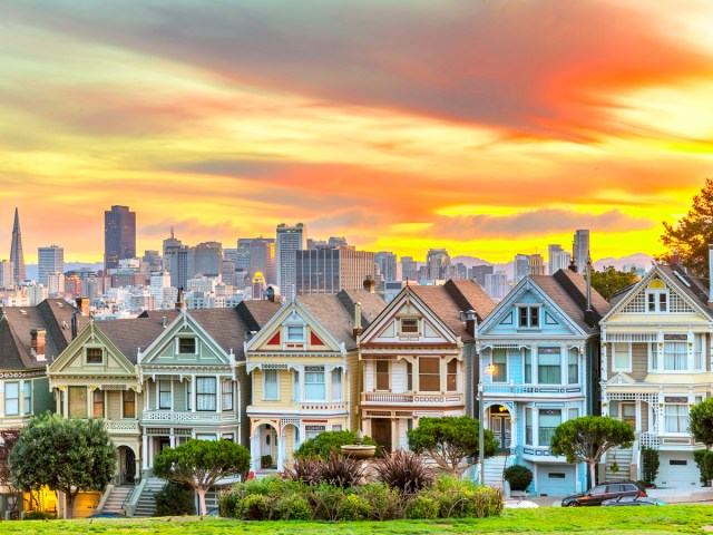 Victorian homes of San Francisco known as the "Painted Ladies," seen at sunset with skyline in background