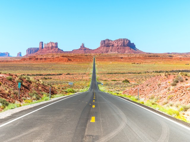 Empty two-lane stretch of historic Route 66 leading toward rock formations in Monument Valley, on the border of Arizona and Utah