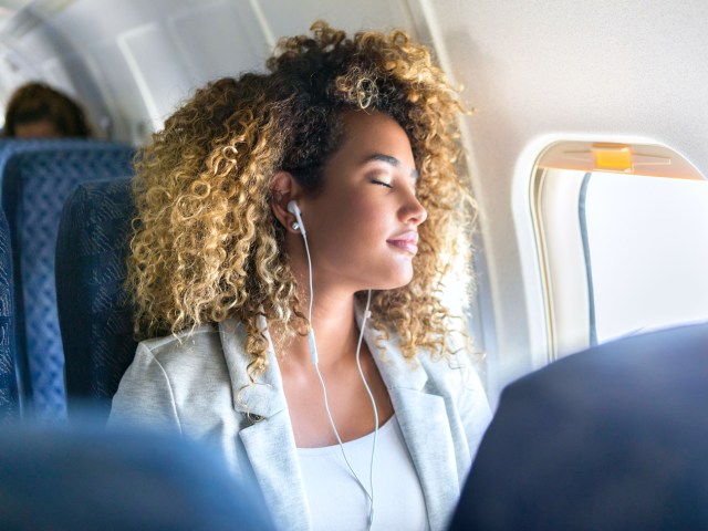 Passenger wearing headphones sleeping in window seat of airplane