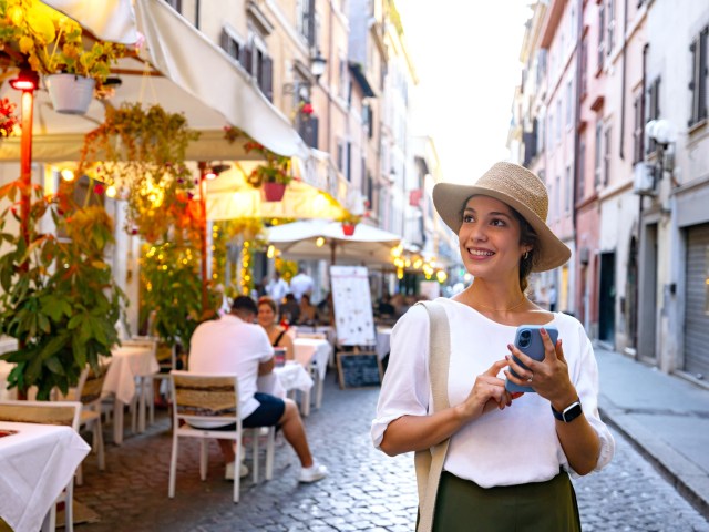 Tourist standing beside sidewalk cafe holding cellphone