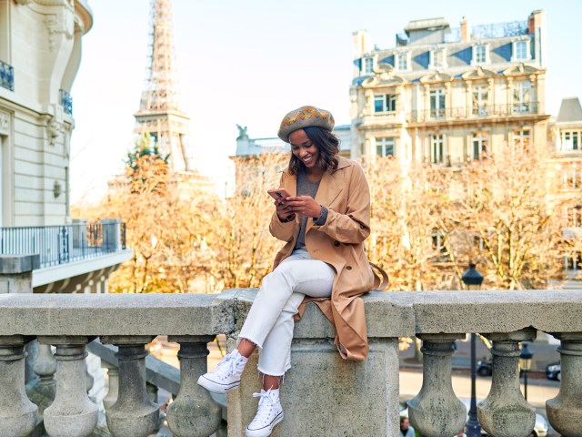 Woman sitting on railing using cellphone