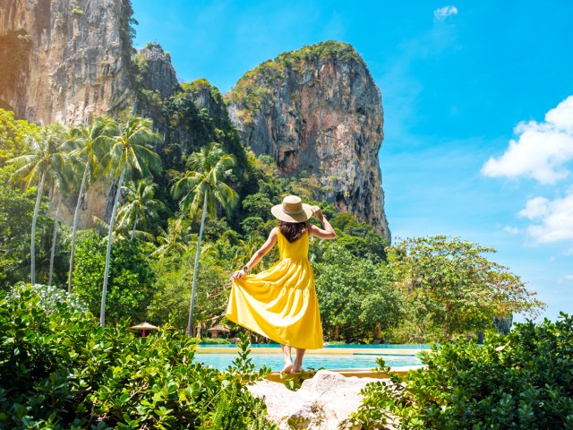 Woman in yellow dress standing by pool admiring rock formations in Krabi, Thailand