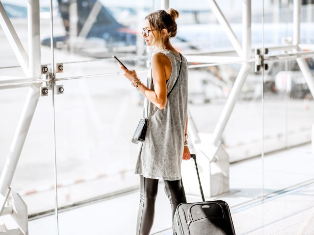 Airline passenger holding phone and luggage next to airport window