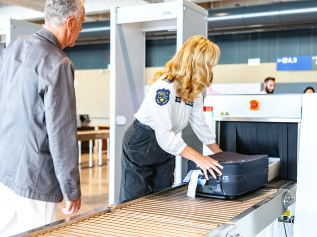 Security officer placing luggage through X-ray machine at airport