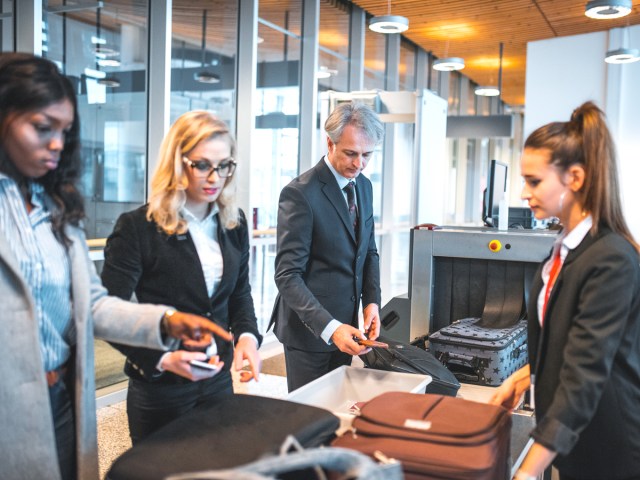 Passengers and employees standing next to security belt at airport