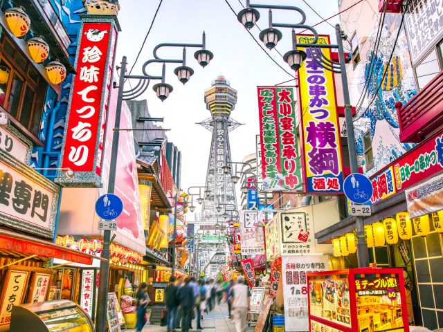 Brightly colored signs along busy pedestrian street looking toward Osaka Tower in Osaka, Japan